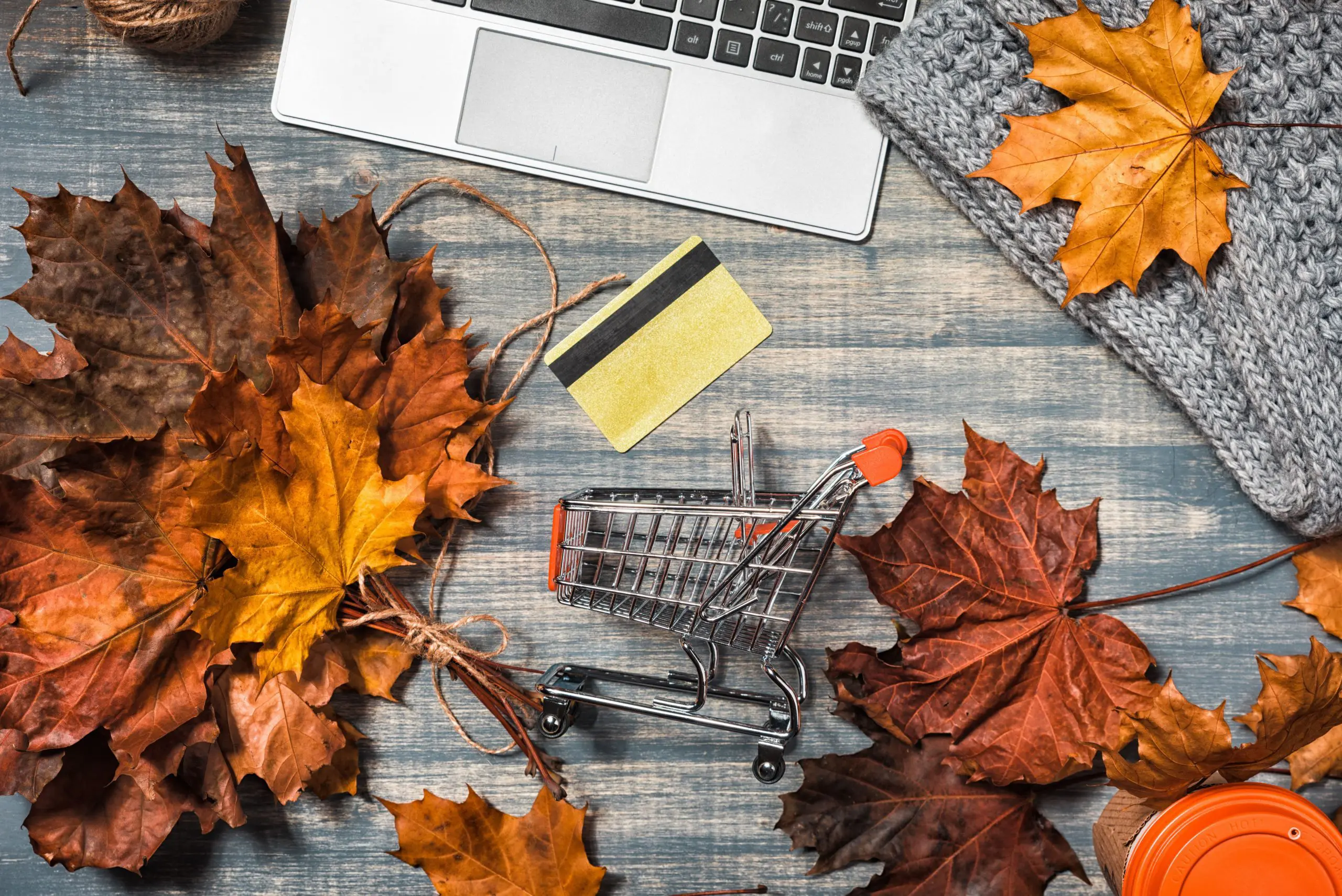 A laptop, card and miniature shopping cart among fallen autumn leaves