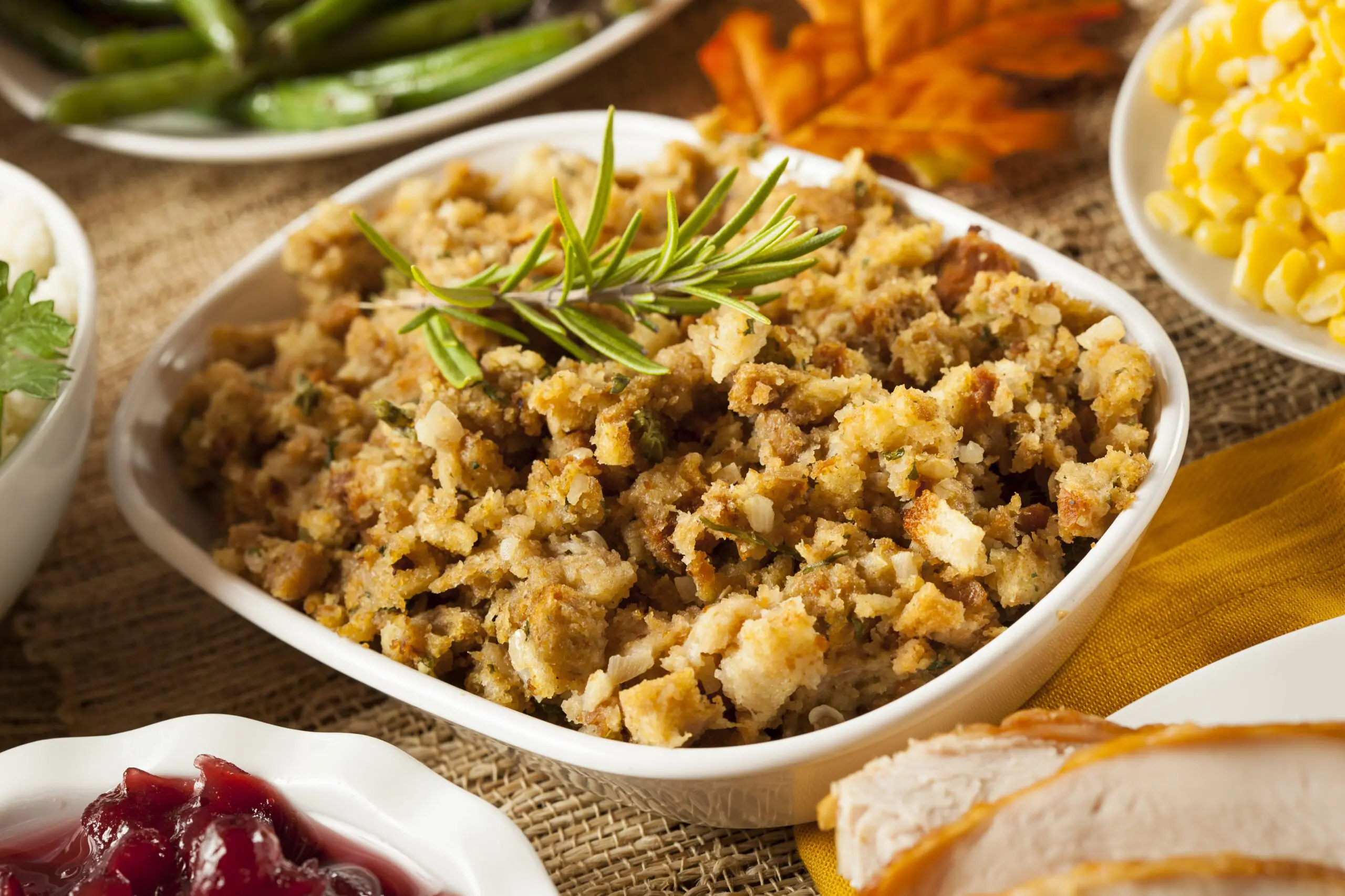 A dish of herbed stuffing surrounded by green beans, corn and cranberry sauce