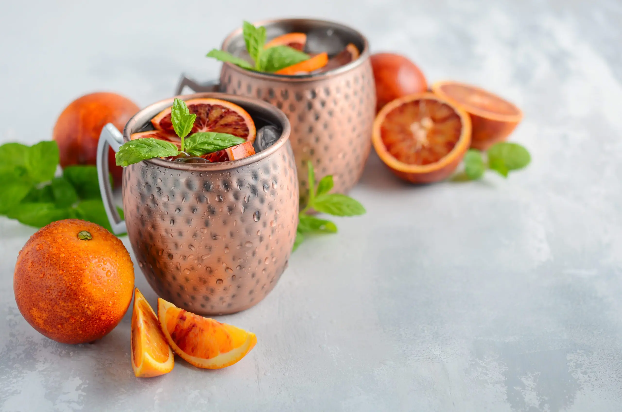 Two copper mugs of Moscow mule garnished with blood orange and mint