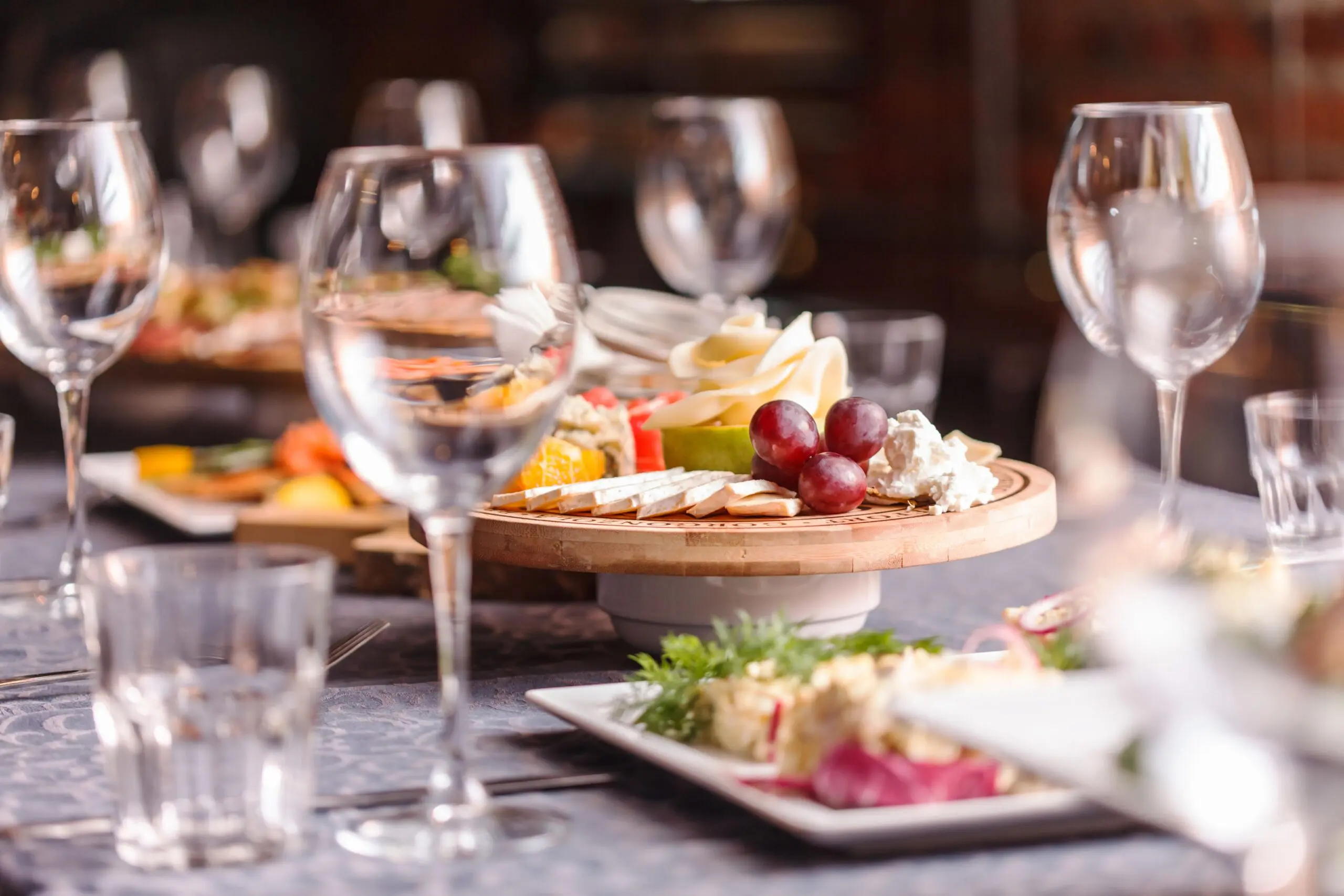 A supper table laid with a cheese and fruit board, wine glasses and small plates