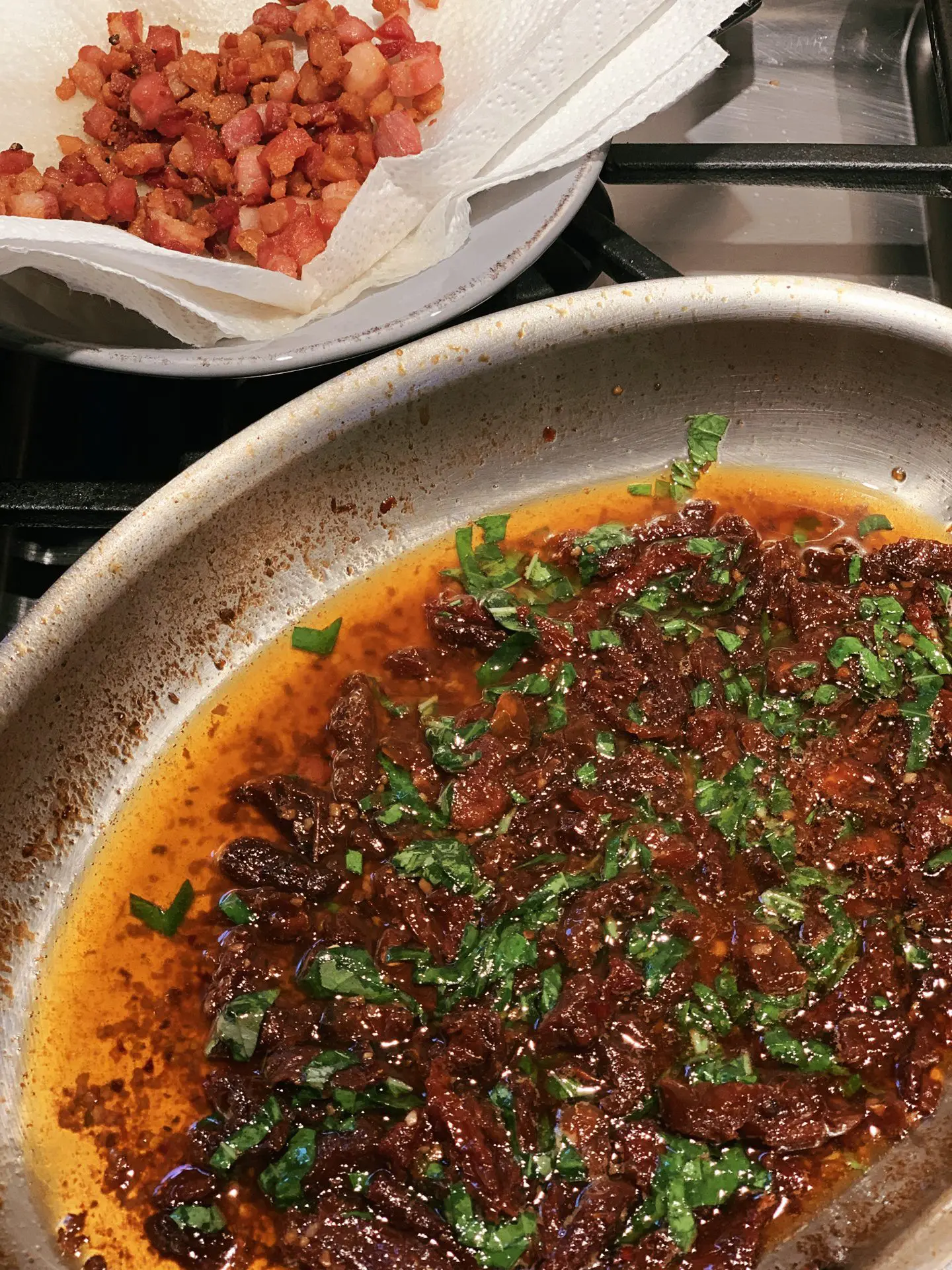 Sun-dried tomatoes and pancetta simmering in a pan, with crisped pancetta draining alongside