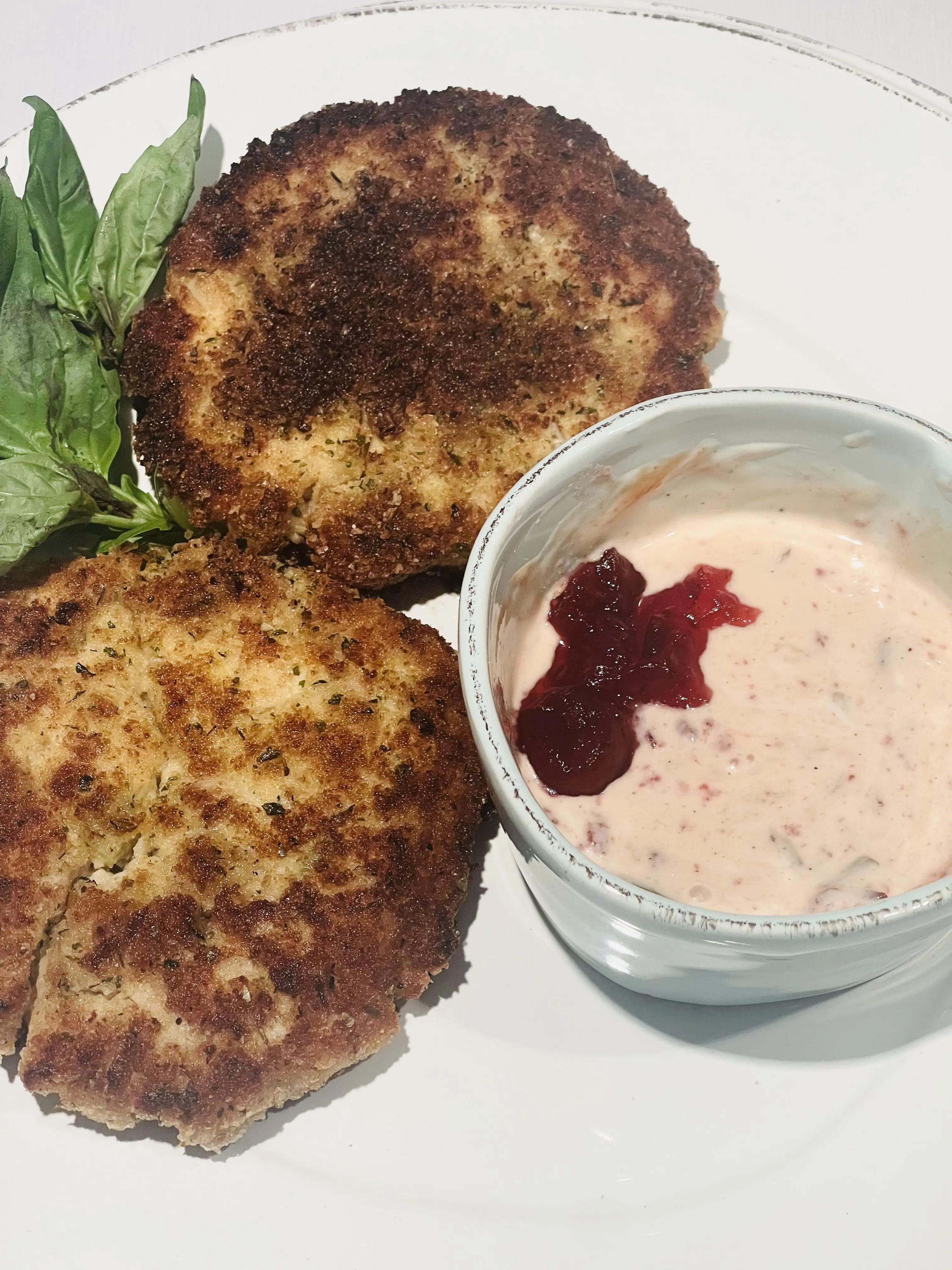 Turkey cakes plated with basil and a bowl of cranberry-flecked sauce