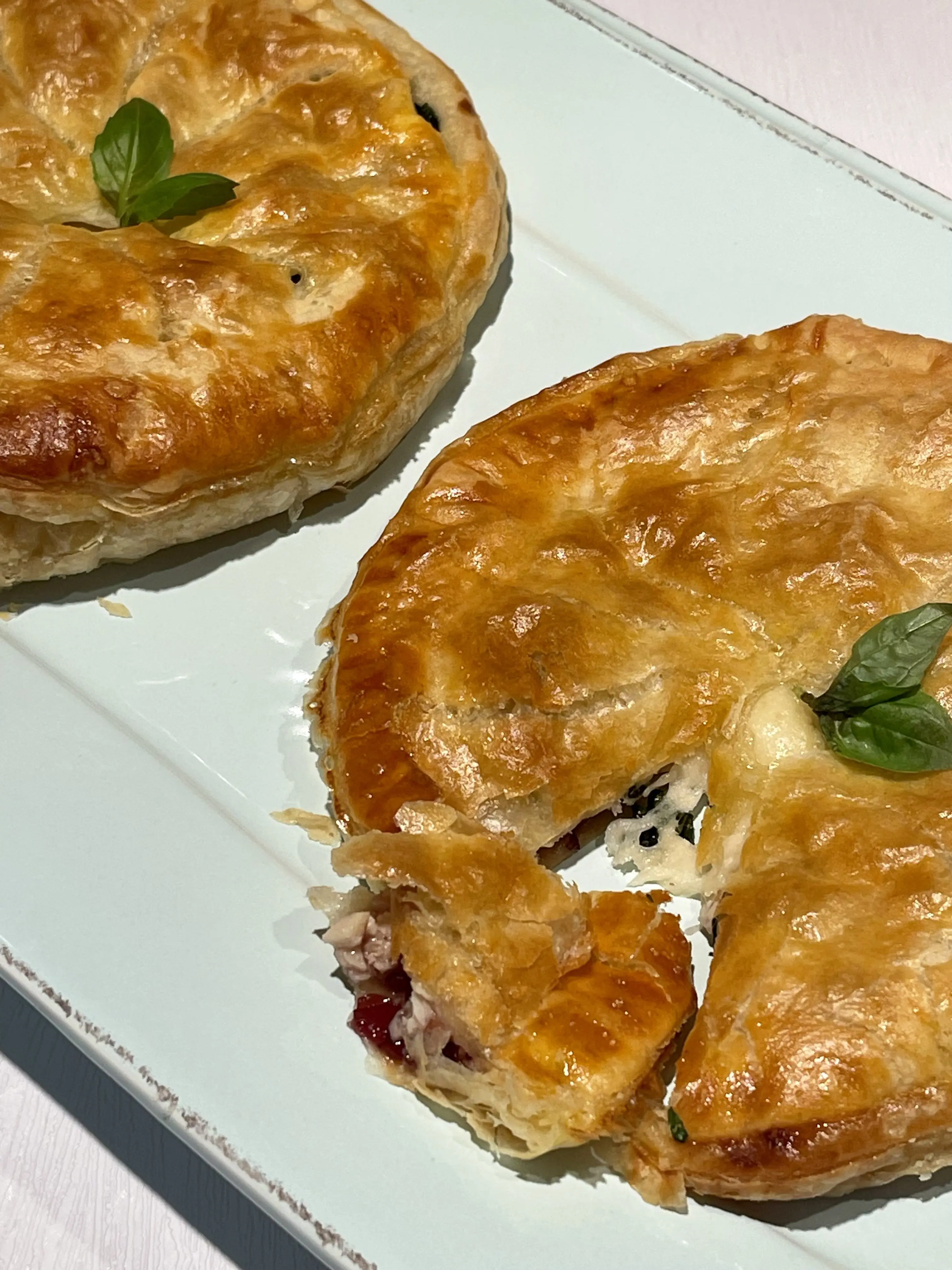 Two golden baked pithiviers on a white platter, one broken open