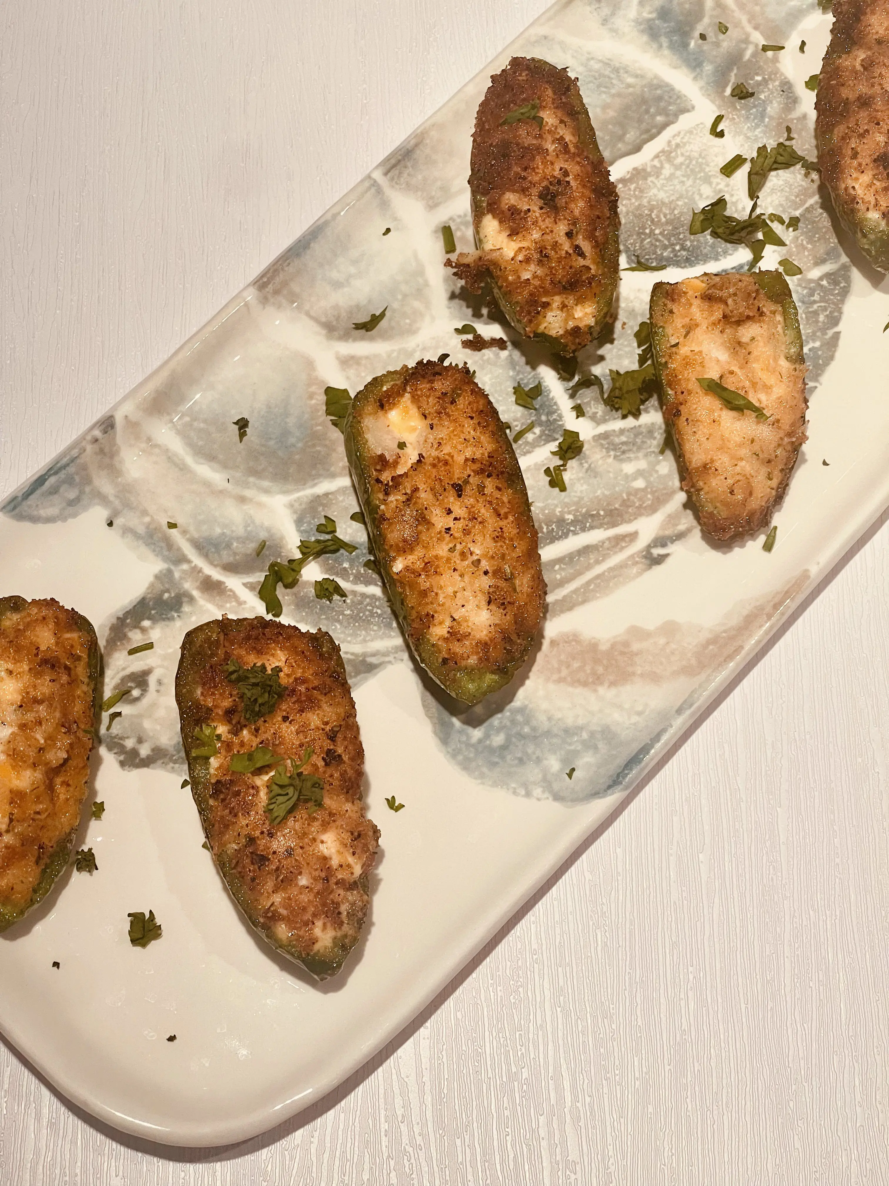 Breaded stuffed jalapeno poppers on a pale ceramic tray