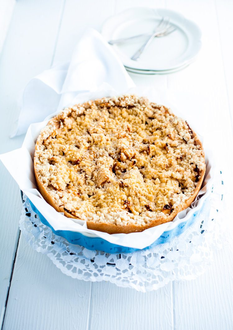 High key image of a delicious fresh baked plum pie on a decorative doily on white boards with plates ready to be served