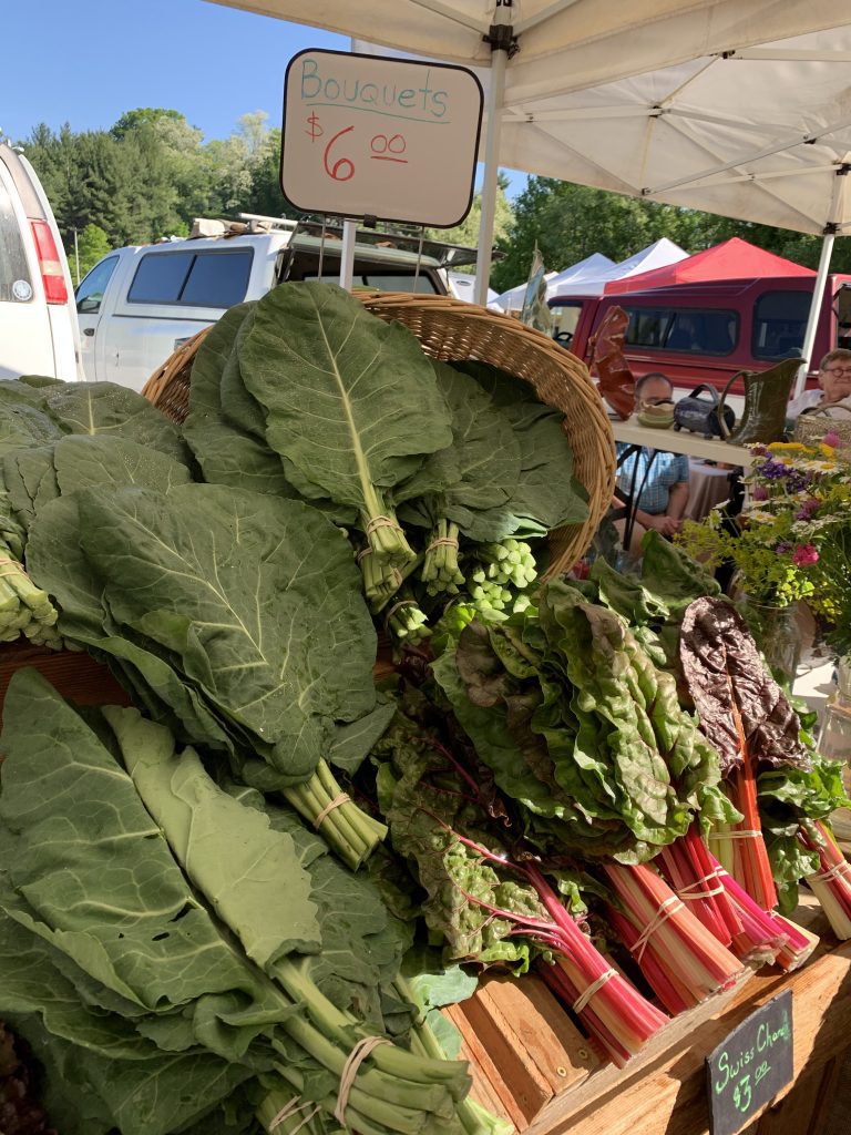 A messy farmers market haul spread out on a marble counter with vibrant green leafy vegetables, radishes, and dark purple onions