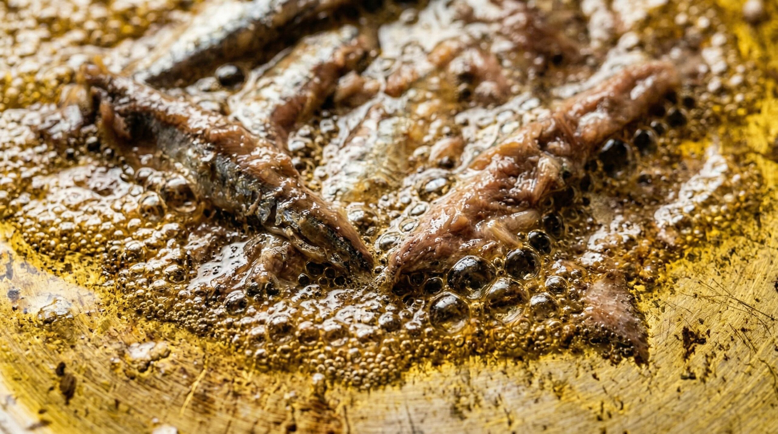Anchovy fillets dissolving into warm olive oil in a skillet to build an umami base