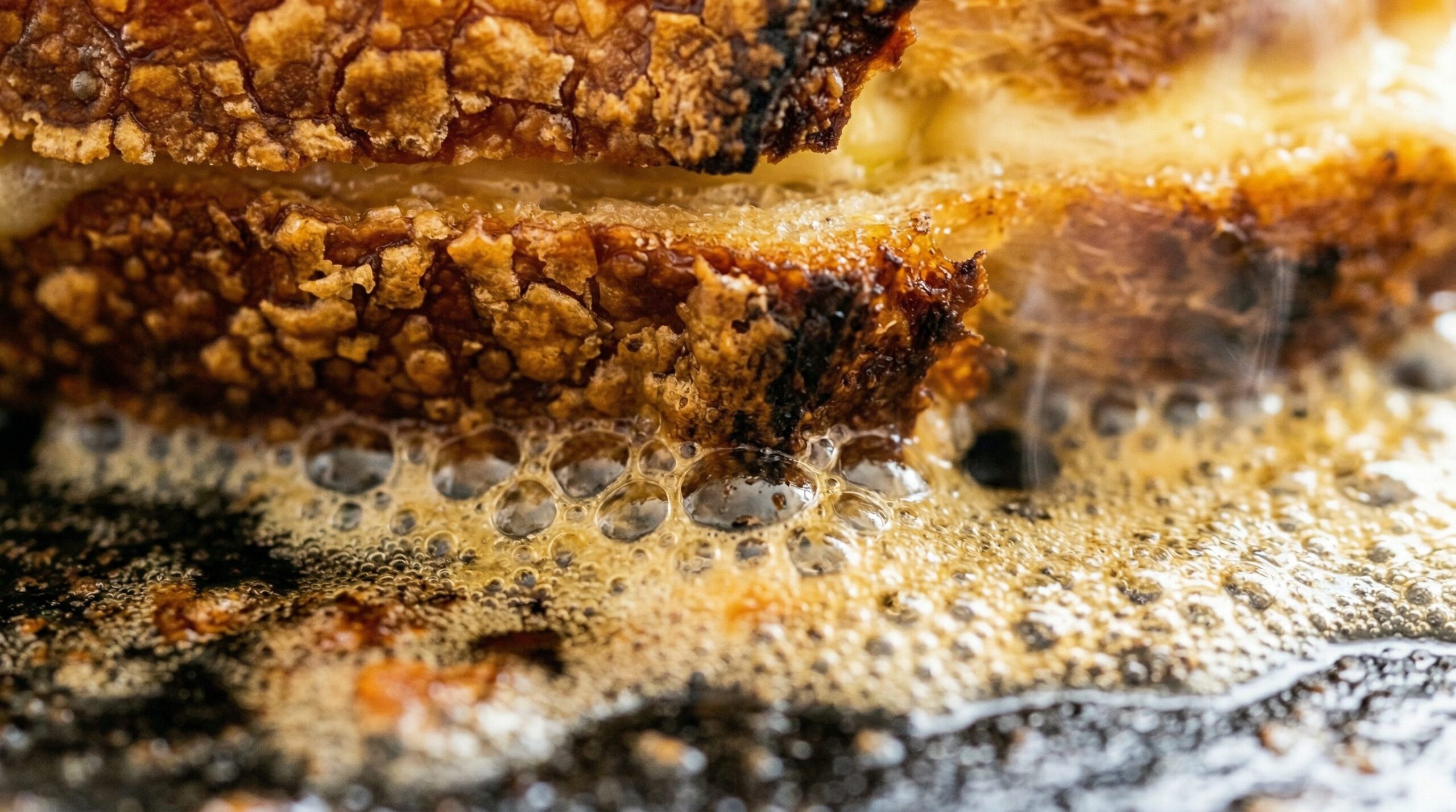 A mayonnaise-crusted grilled cheese searing in foaming butter in a cast-iron skillet